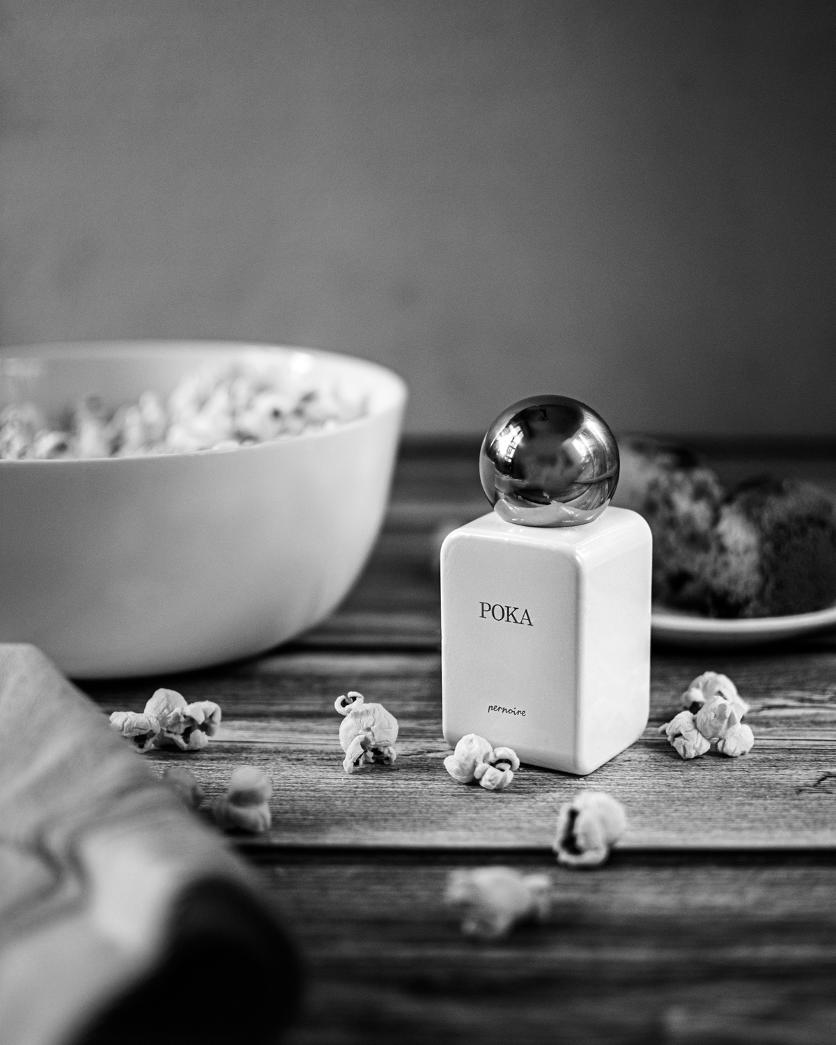 White POKA bottle on a dark wooden table with scattered popcorn beside a white bowl.
