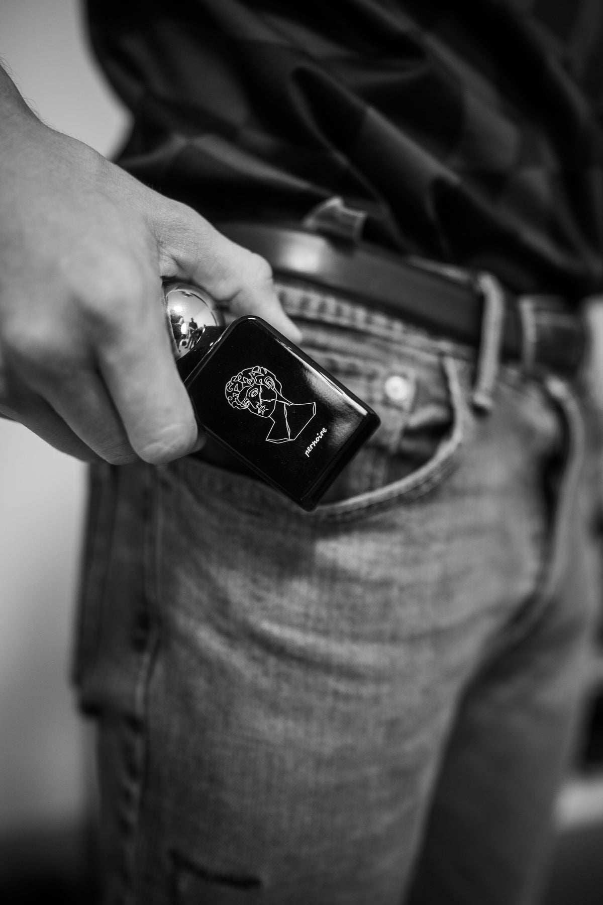A hand holds the black AMORAL bottle with its line illustration beside a dark shirt and denim jeans.