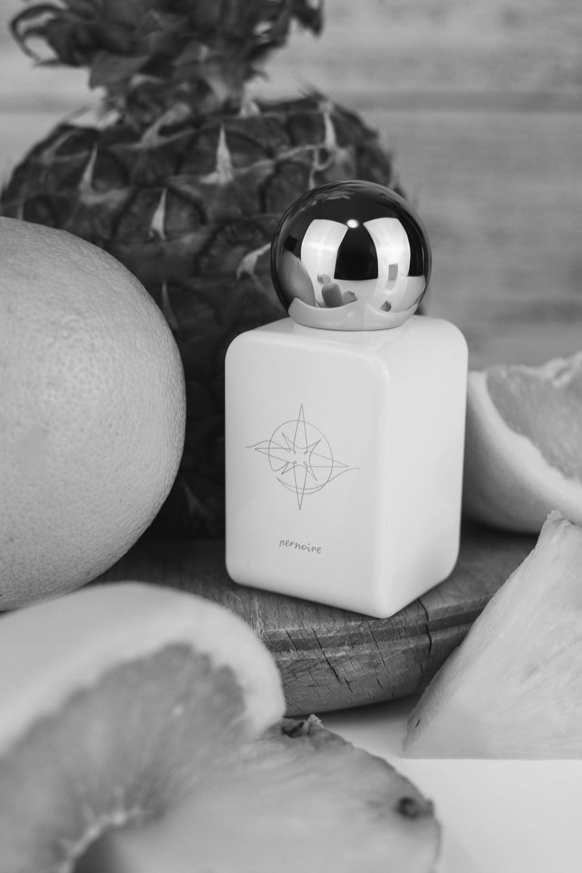 White ANELO bottle with its compass illustration among cut tropical and citrus fruits.