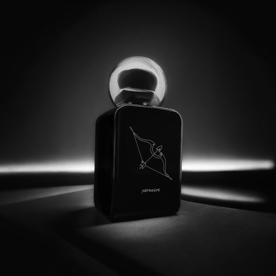 Black KAMA perfume bottle by pernoire with a bow-and-arrow illustration against a dark background and narrow beam of light.