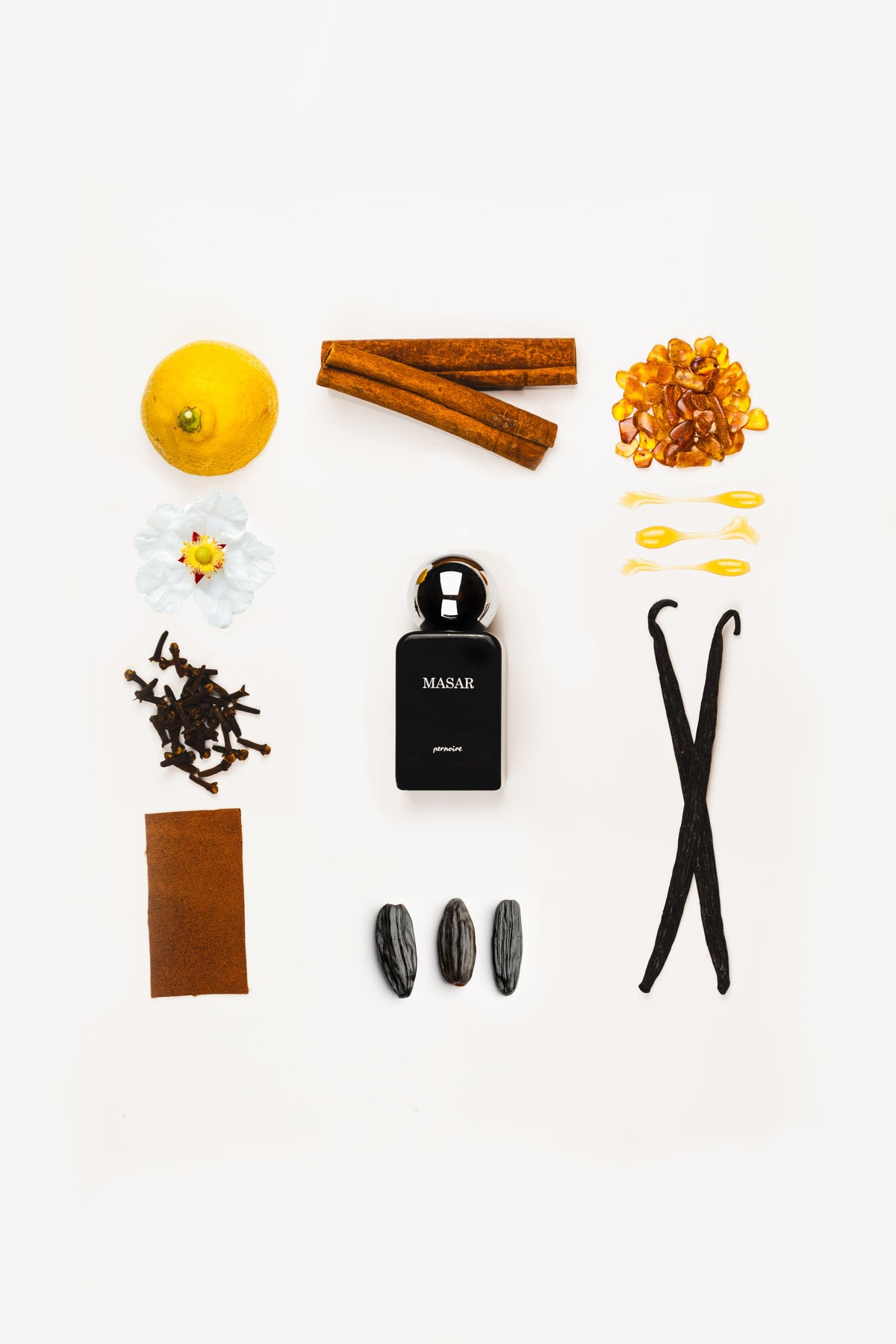 Black MASAR bottle surrounded by citrus, cinnamon, vanilla pods and other fragrance materials on white.