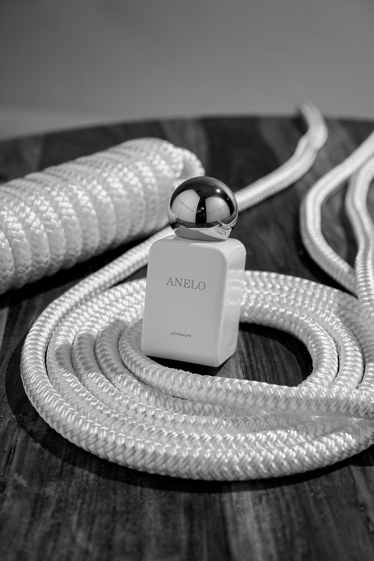 White ANELO bottle on dark wood beside thick coils of rope.