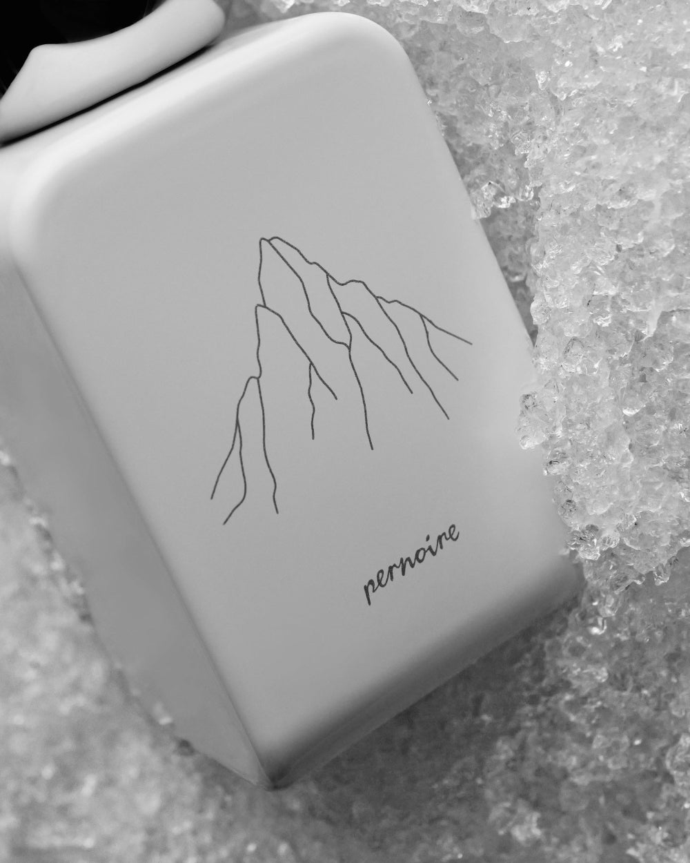 Nahaufnahme des Bergmotivs auf dem weissen YUMA-Flakon von pernoire in zerkleinertem Eis.