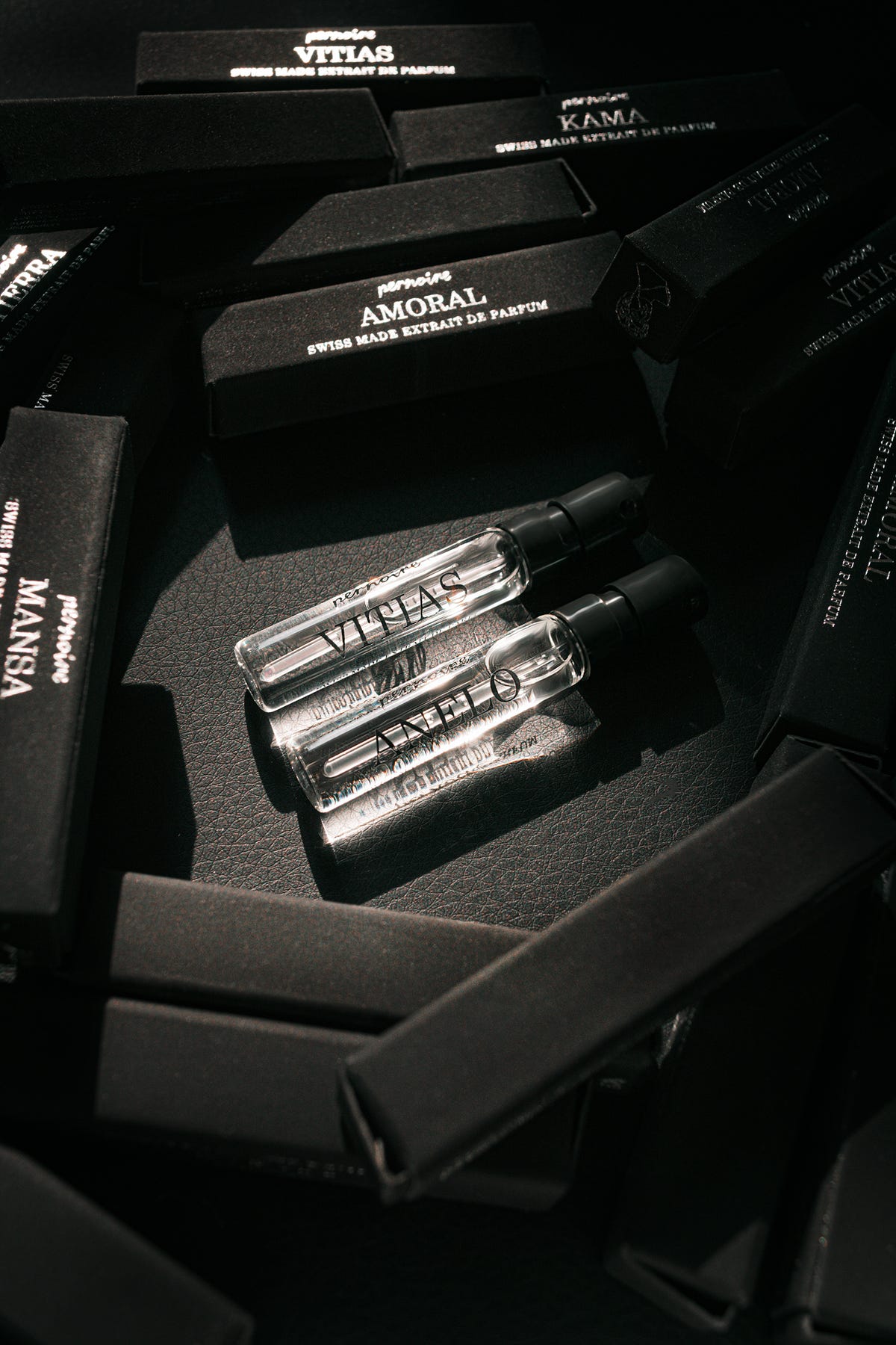 Anelo and Vitias perfume sample sprays on black pernoire sample packaging.