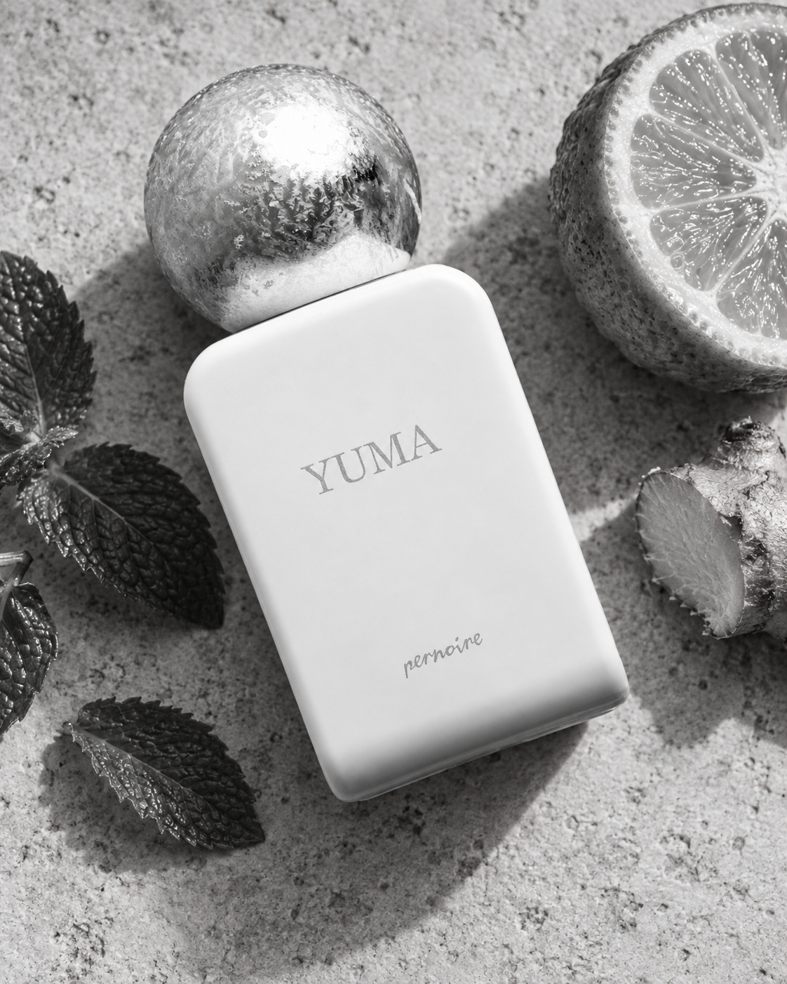 White YUMA bottle with mint leaves, cut citrus and ginger on pale stone.