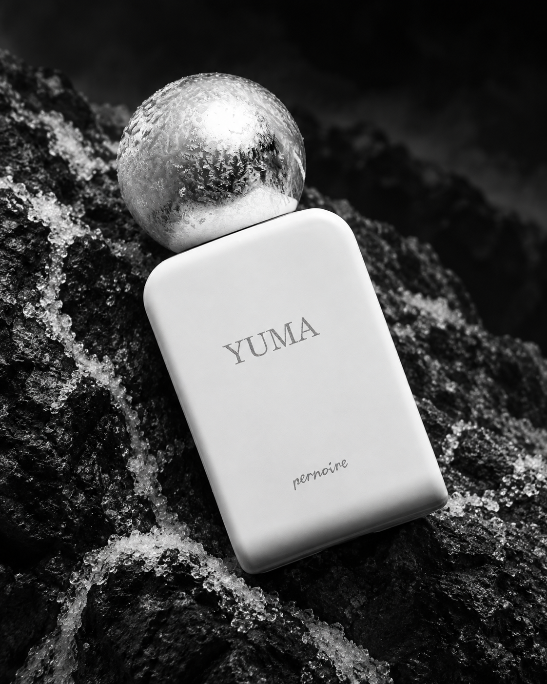 White YUMA bottle with a frosted cap, lying diagonally among dark rocks and traces of ice.